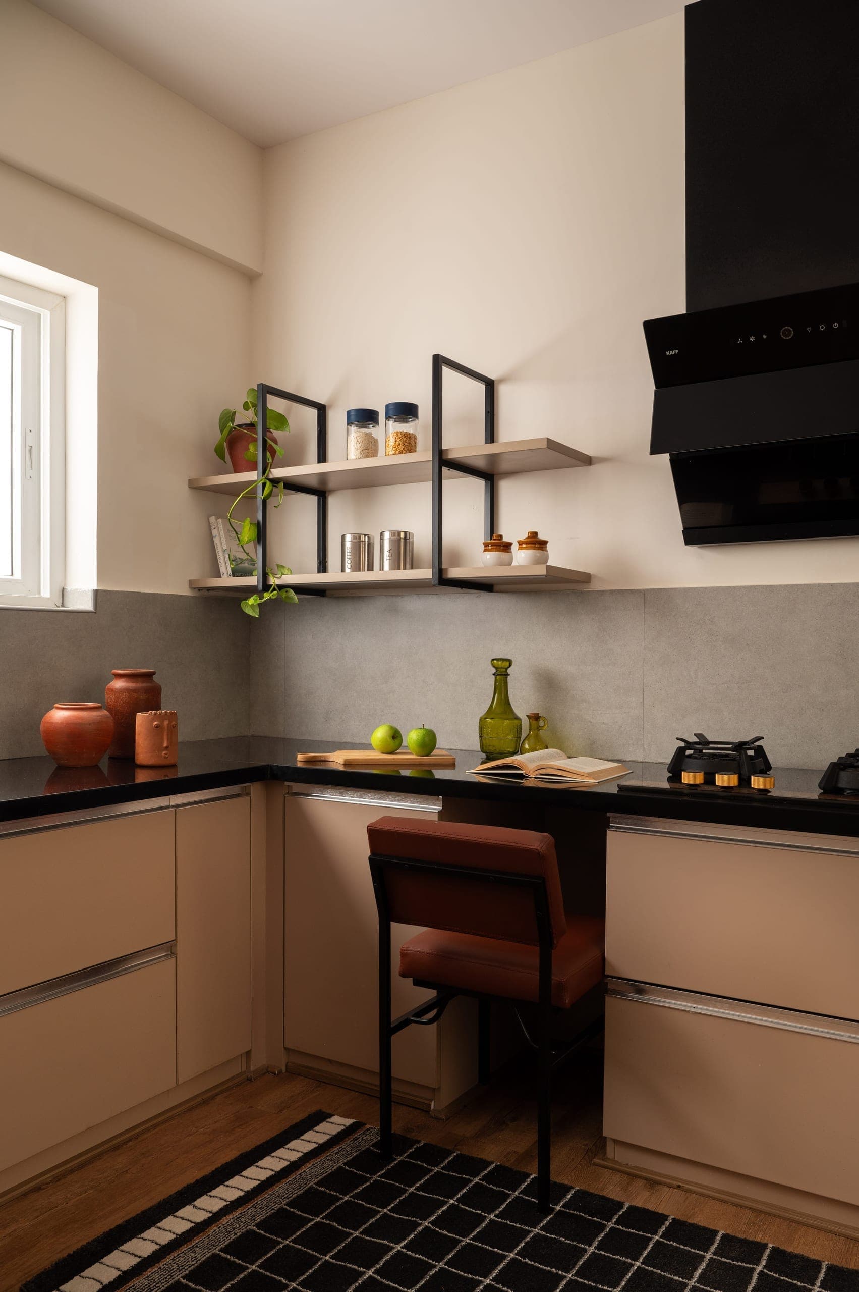 The kitchen was redesigned with ergonomics at its core. Lower counter heights reduce reach and strain during extended use. A built-in counter with a high stool offers a comfortable perch for food prep—small in gesture, significant in impact. Warm almond-finish cabinetry lines the perimeter, paired with matte black stone counters. Open steel shelving replaces overhead cupboards, keeping essentials within easy reach. A cool grey micro-cement splashback completes the palette.