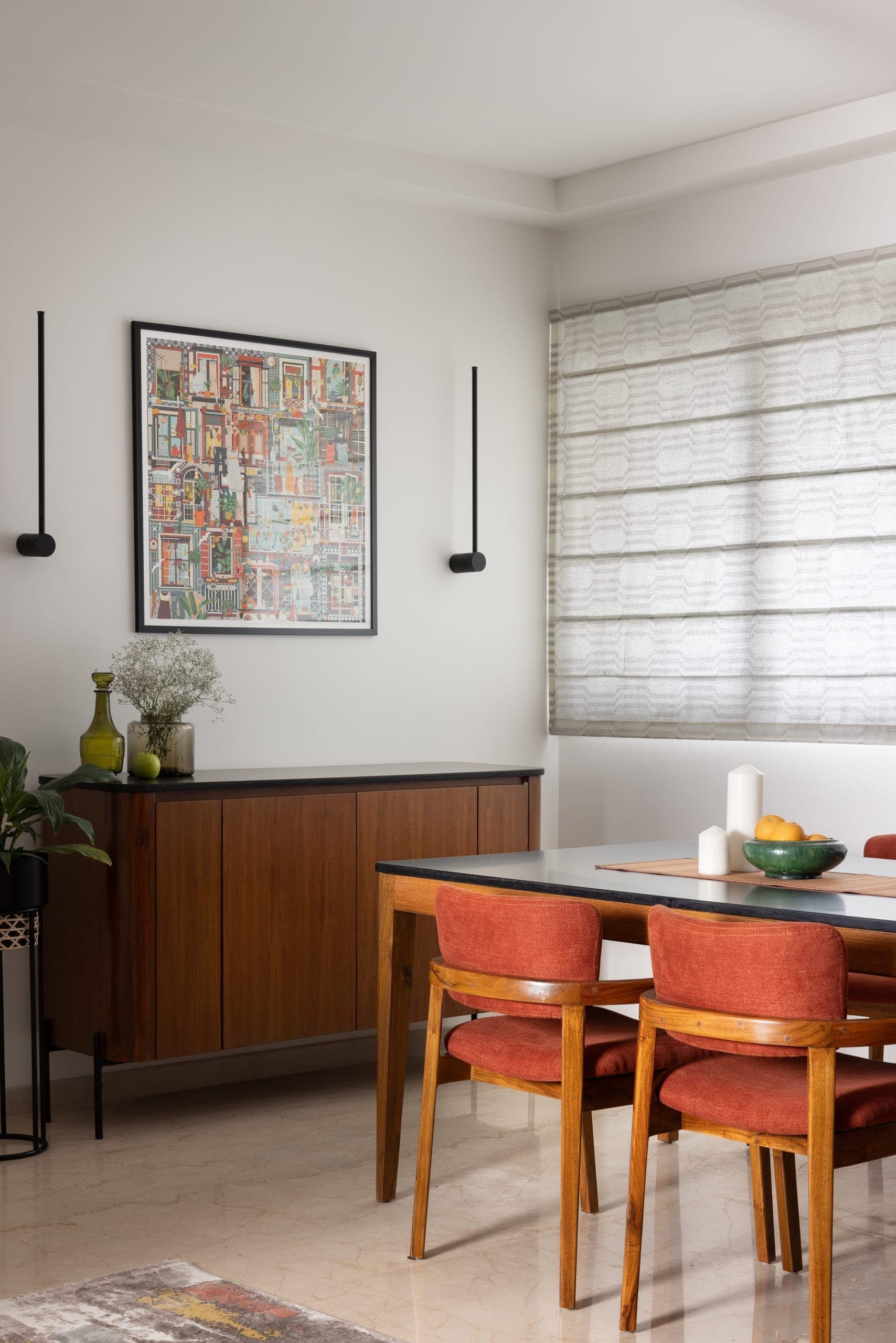 A teak table with a dark stone top anchors the space against a white wall, with rust-orange chairs adding warmth.