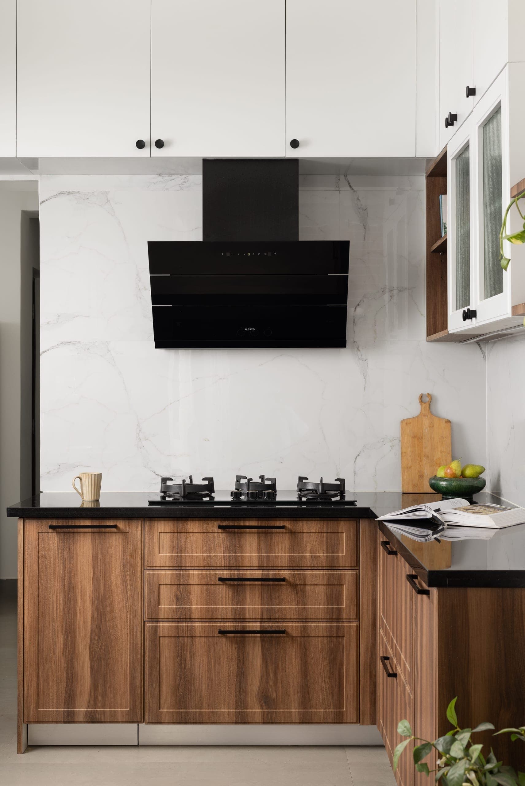 The membrane-finish kitchen is kept simple, with Shaker-style base shutters and wall units in white frames with ribbed glass. Black granite countertops paired with a Statuario backsplash bring the palette together.