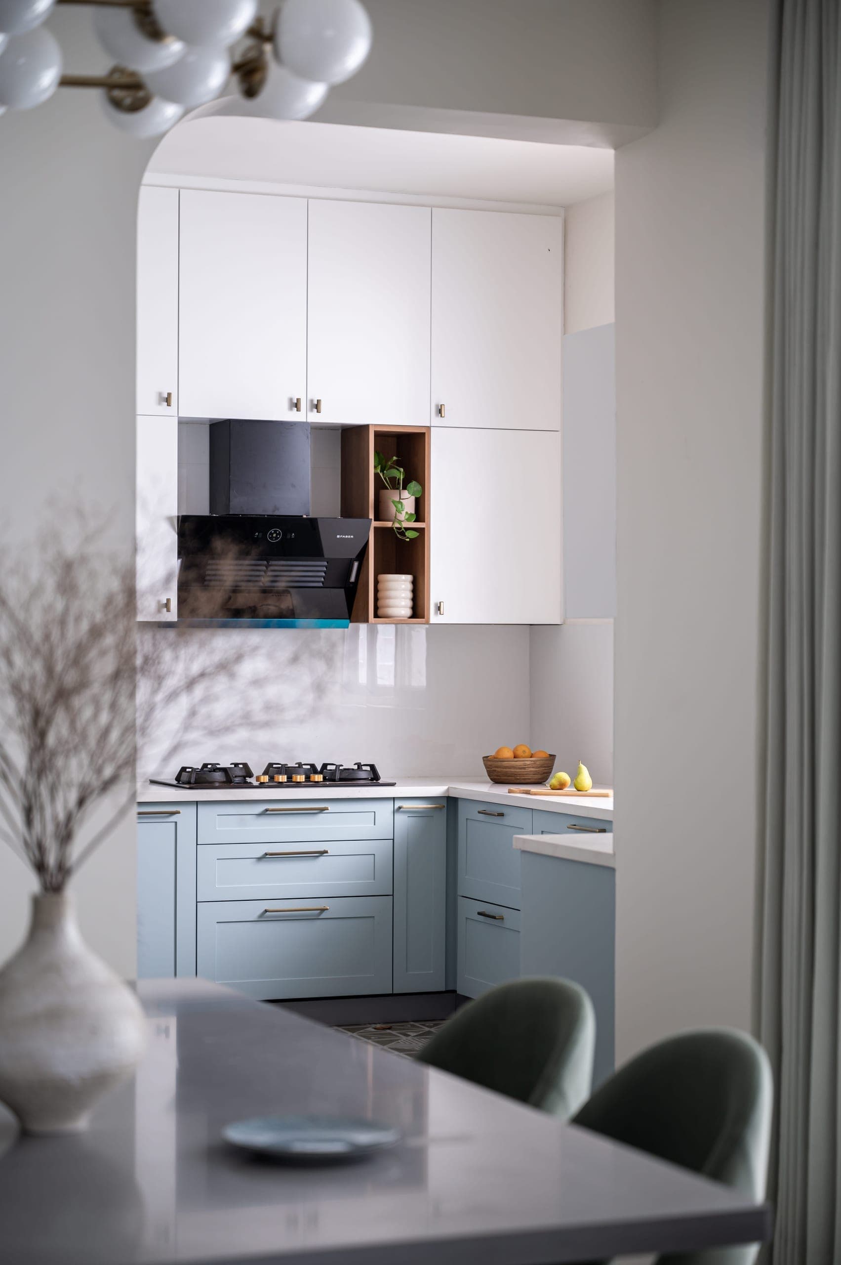 Adorned with a tasteful palette of powder blue and pristine white, the cabinetry exudes a sense of serene sophistication. The floor becomes a canvas of intricate patterns, thanks to meticulously chosen tiles that add a touch of artistic flair to the culinary space.
