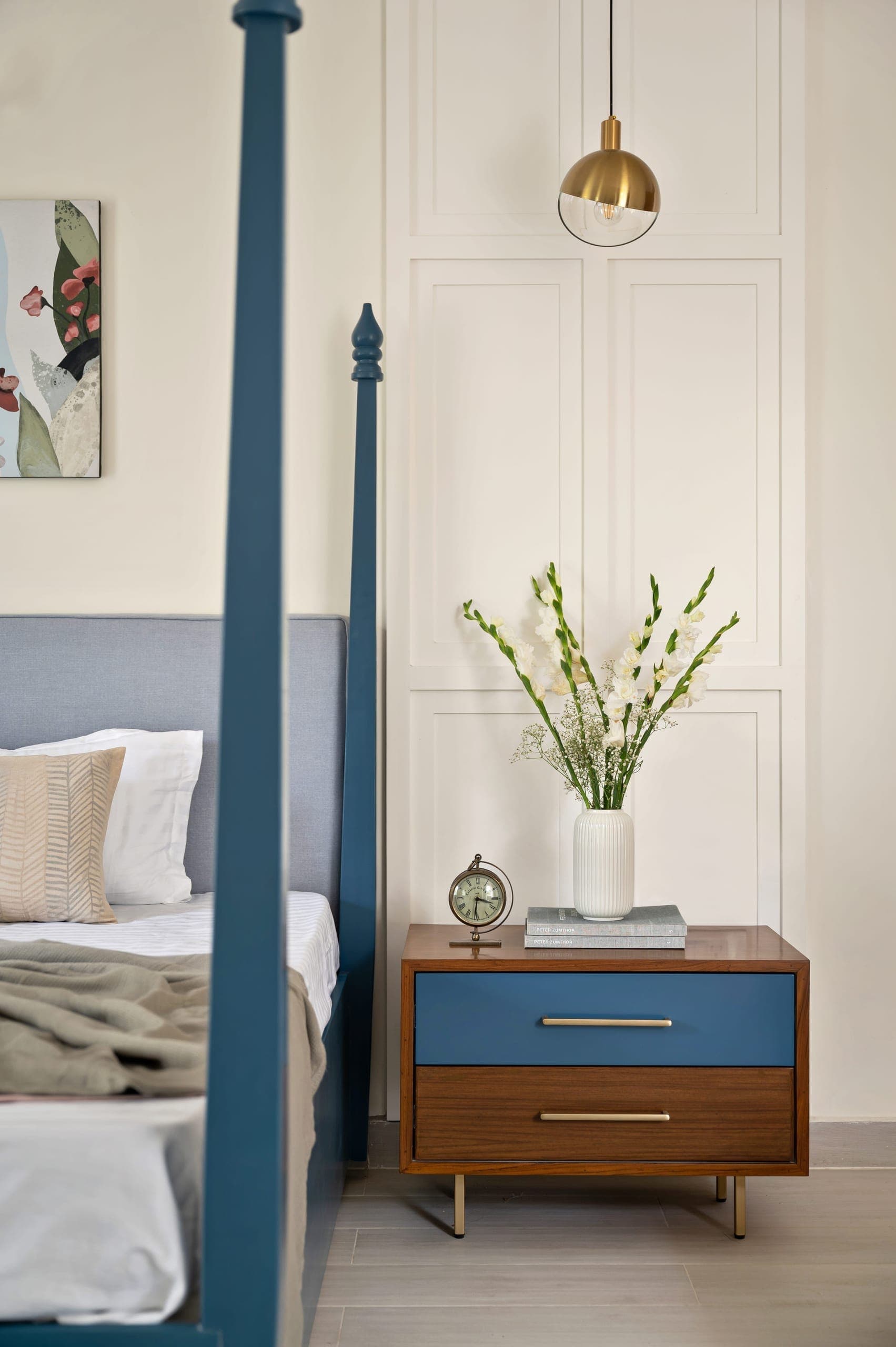 The master bedroom is anchored by a four-poster bed in a muted blue, setting the tone for the space. Creams and warm wood form the base palette, with blue accents carried through in a restrained way.