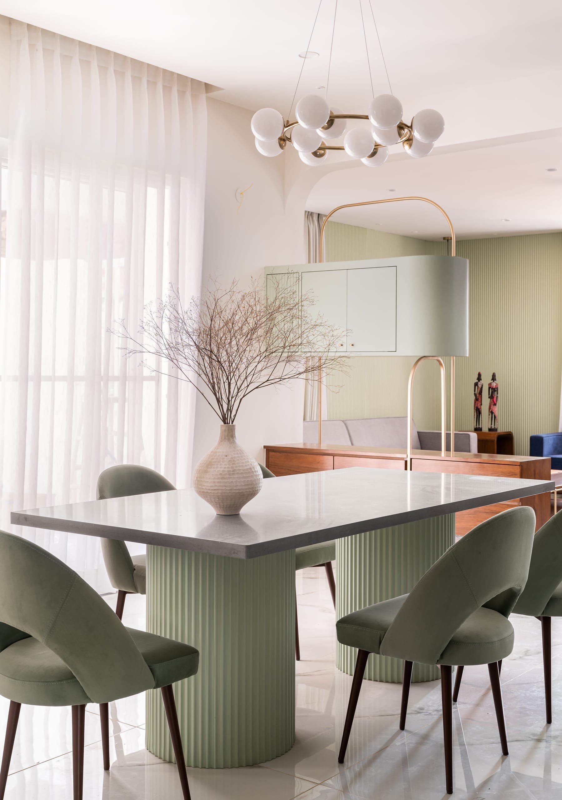 In the dining area, a sculptural table anchors the room, complemented by a chandelier that adds focus and soft light. Together, these elements create a setting that is simple, refined, and well-composed.