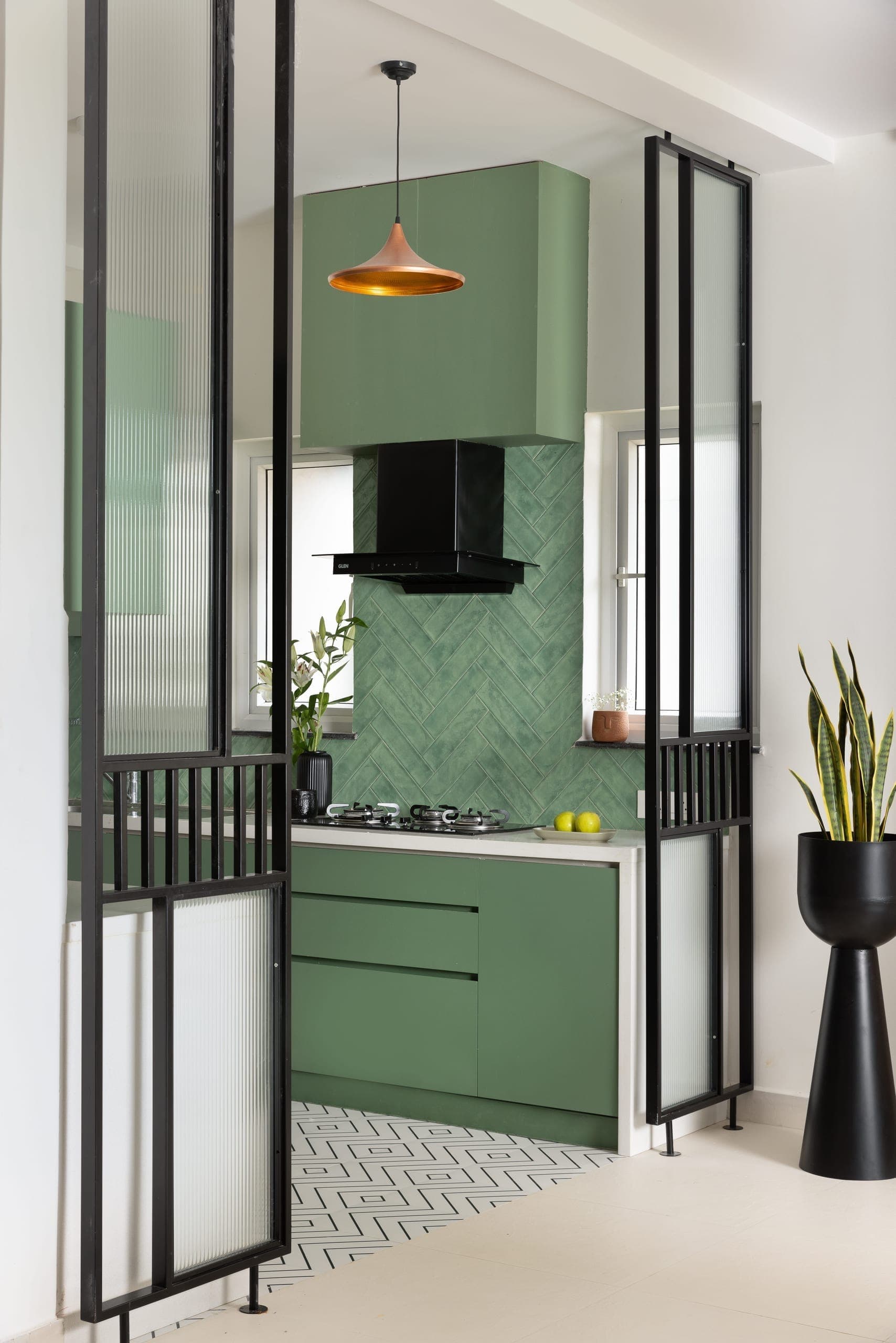 The kitchen is defined by muted green cabinetry and textured tiles, framed by fluted glass partitions that keep the space open yet contained.